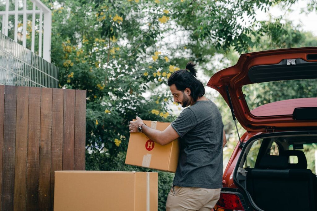 Young male taking boxes out of luggage boot of car